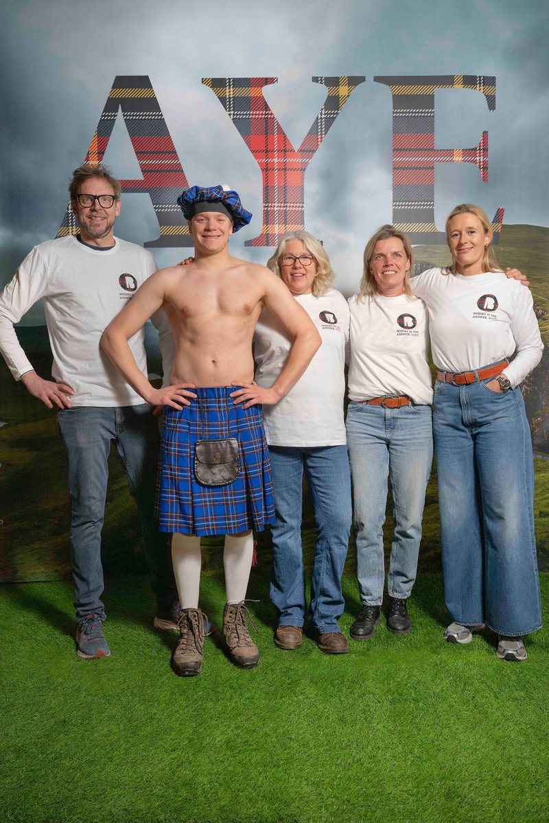 The crew in front of a tartan AYE backdrop, one of them in a kilt
